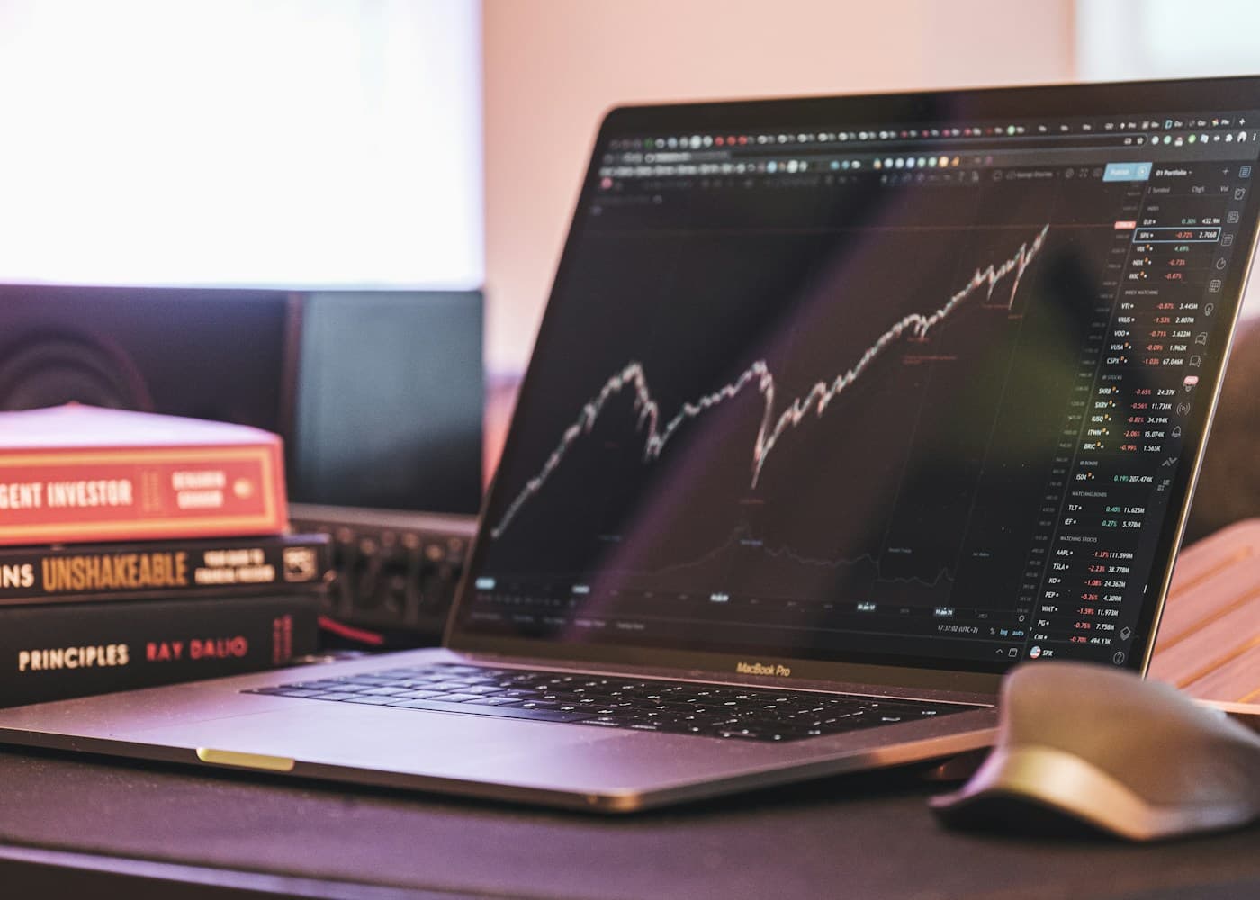 Laptop showing trading charts beside investing books
